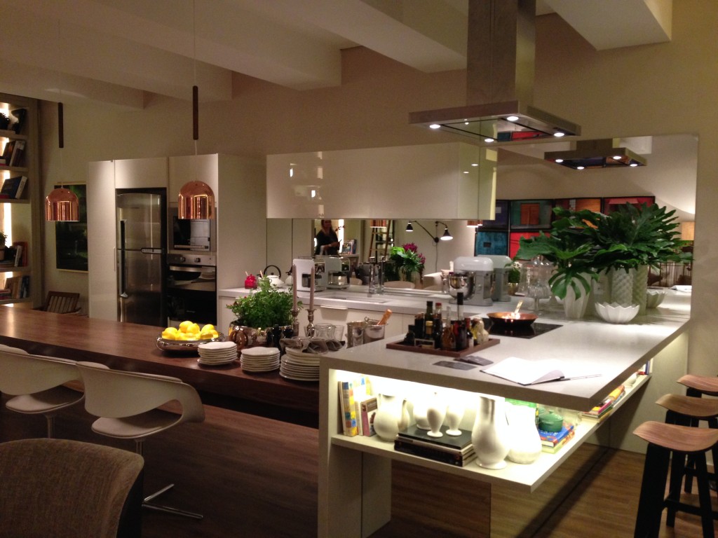 A cozinha, aberta, está integrada com o ambiente. A bancada funciona como bar e mesa de jantar, rodeada de bancos com design assinado do arquiteto Jader de Almeida.