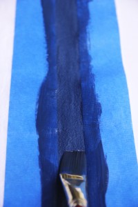 Com o pincel, pintar o espaço entre as fitas adesivas e esperar secar com a fita ainda colada na toalha.