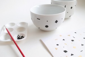 Pinte o papel com a tinta preta primeiro, e enquanto a tinta estiver molhada, envolva a xícara, pressionando o papel contra ela, sem borrar. 