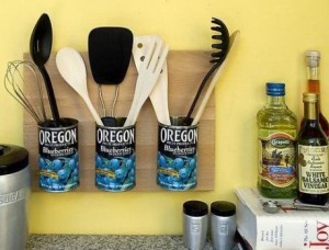 Usar latas usadas presas a uma tábua de madeira como porta utensílios de cozinha é bem original!