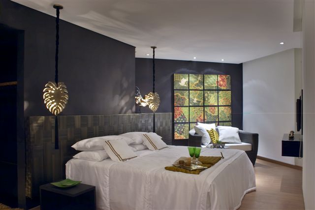 A Suite 501, super contemporanea, foi pensada por Ana Paula Massot Rohlfs. Mesmo com elementos alegres, como a montagem com os quadros na parede de fundo e os pendentes sobre as mesas laterais, o quarto nos transmite uma sobriedade, pelo uso de cinza escuro nas paredes. A descontrção vem da cabeceira trançada da cama e a generosa namoradeira com os quadros coloridos ao fundo!